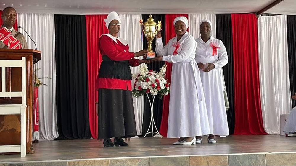 Bulawayo HQ choir members in white receive a gold trophy on stage at the 2023 competition