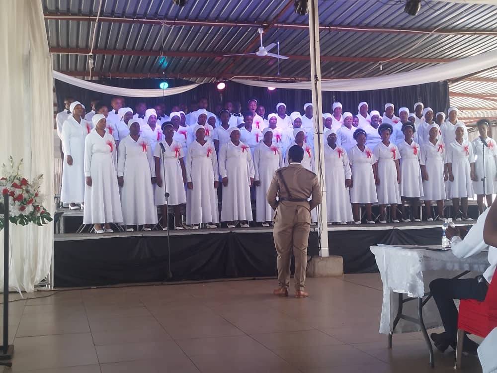 A choir in white on stage, with the conductor in front